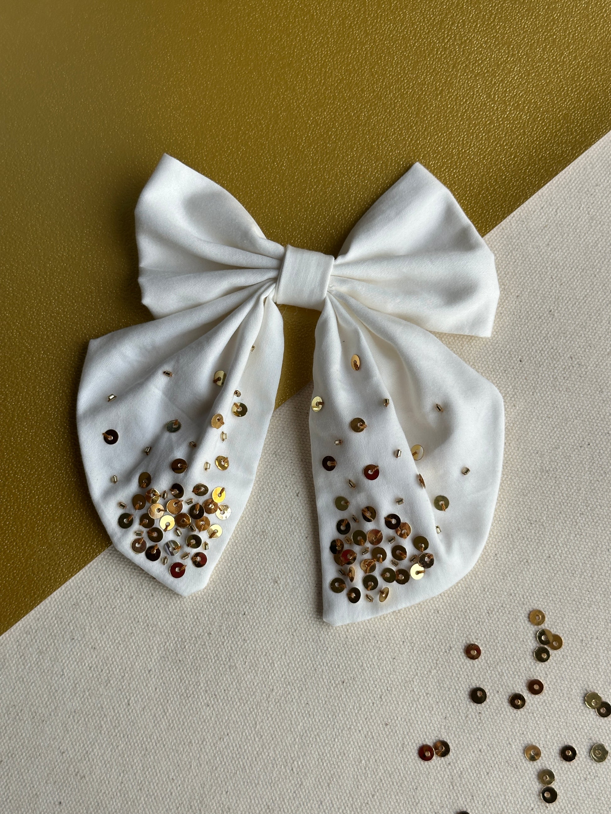White bow with gold and brown sequins on a beige background